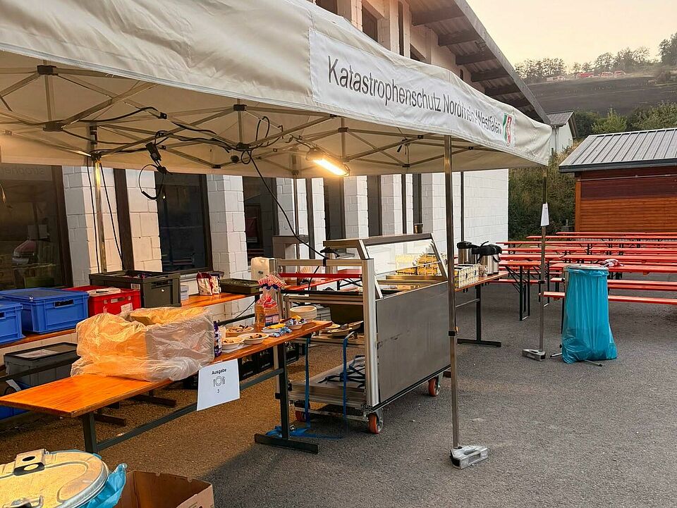 Verpflegung Die mobile Küche der SEG Verpflegung des DRK Brilon ist unter einem großen Zelt aufgebaut.Im Hintergrund sind noch Bierbänke mit Tischen zu sehen.
