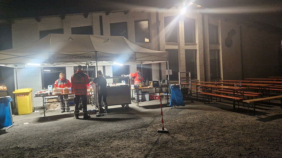 Verpflegung nachts Es ist dunkel. Vor der mobilen Küche des DRK Brilon stehen Einsatzkräfte, die sich etwas zu essen und zu trinken holen.