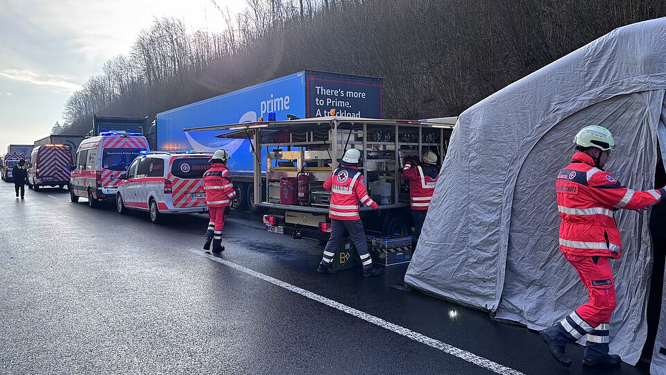 3397 Auf der Bundesautobahn 44 in Fahrtrichtung Kassel, wurde ein beheiztes Zelt aufgebaut. Man sieht 4 Einsatzkräfte von DRK und Johanniter, an einem Einsatzfahrzeug. Es stehen weitere Einsatzfahrzeuge im Hintergrund und ein LKW von Amazon