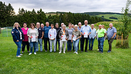 Gruppenfoto von geehrten Blutspenderinnen und Blutspendern aus dem Stadtgebiet Winterberg, die im Rahmen einer Veranstaltung für ihre langjährige Blutspendebereitschaft ausgezeichnet wurden. Mehrere Personen halten ihre Urkunden in den Händen, im Hintergrund ist eine grüne Wiesenlandschaft mit Bäumen und Hügeln zu sehen.