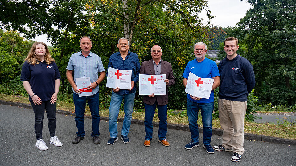 Fünf Blutspender werden bei der Blutspenderehrung 2025 im Stadtgebiet Marsberg für ihre langjährige Treue ausgezeichnet. Sie halten Urkunden in den Händen, flankiert von zwei DRK-Vertretern.